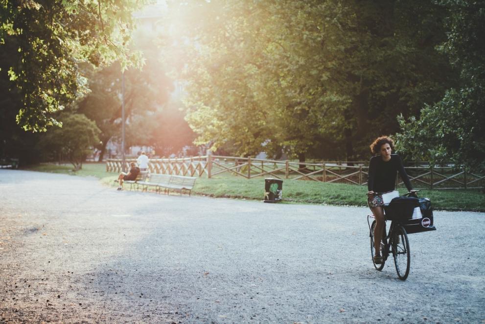 Woman riding her bike in a park with sun coming through the trees